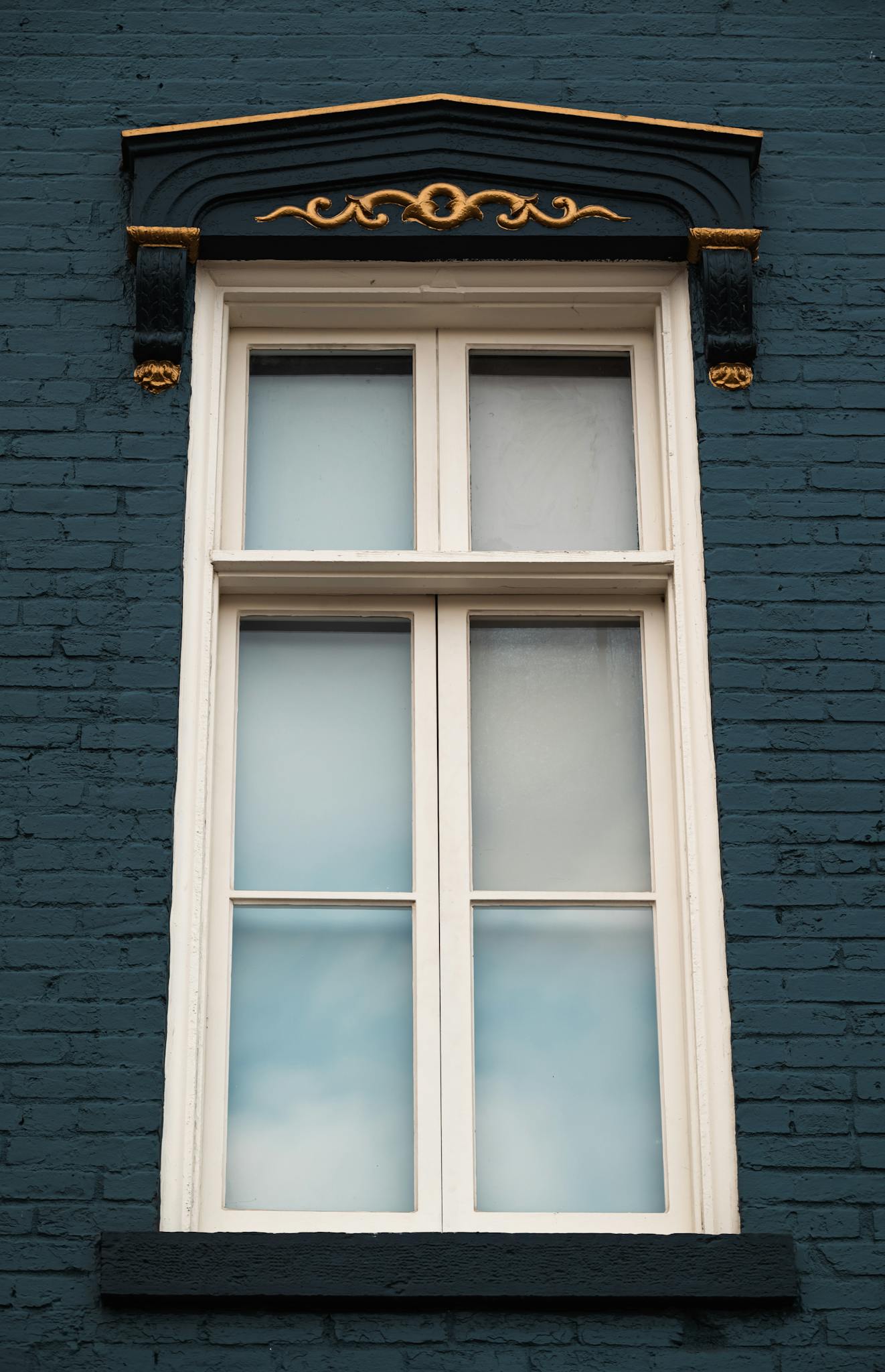 Close-up of a detailed Victorian window on a dark brick wall with ornate designs.